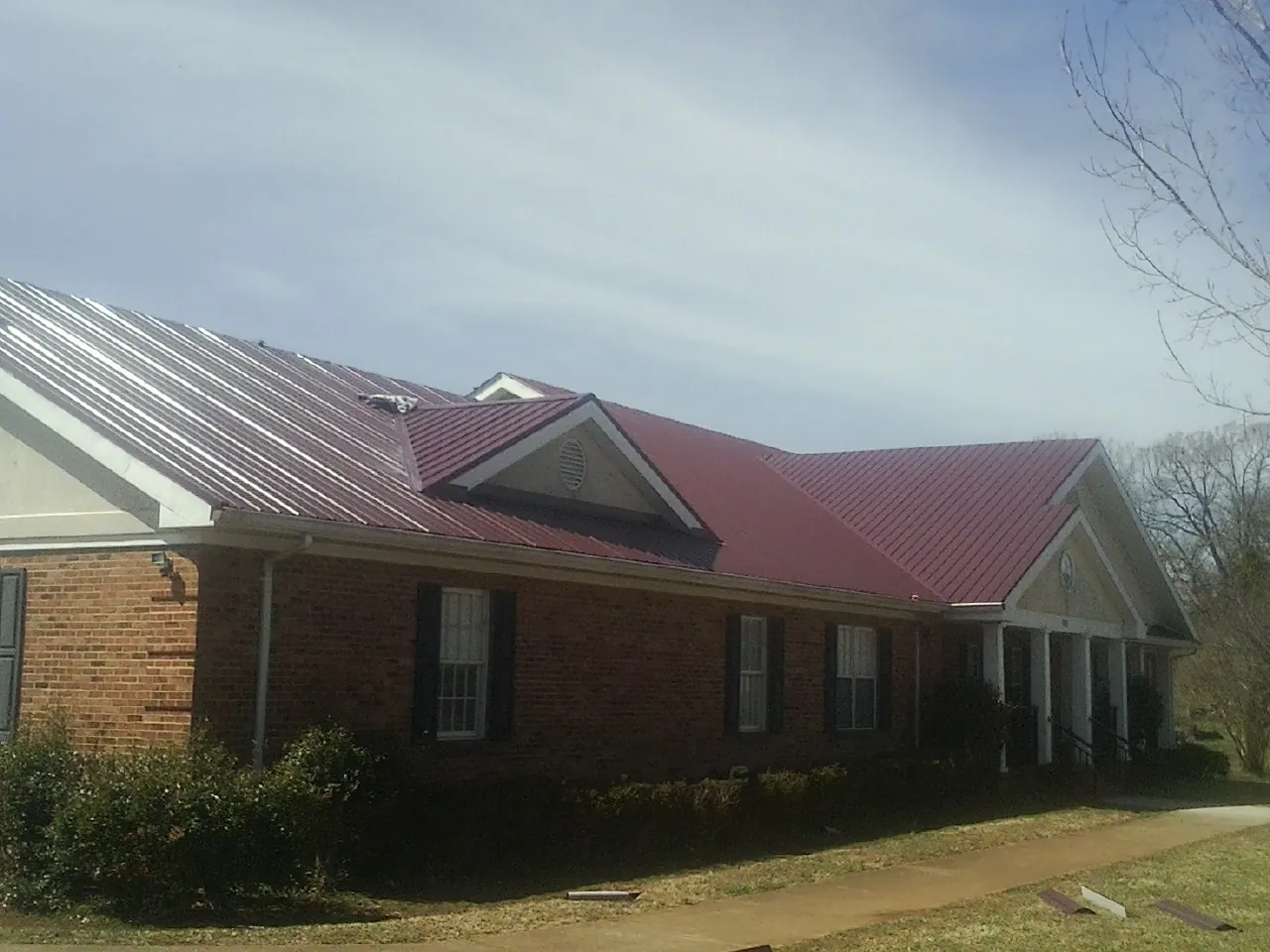 Red metal roof with gabled entries on a long brick building, from a Hail Damage Roof Repair job in Wernersville