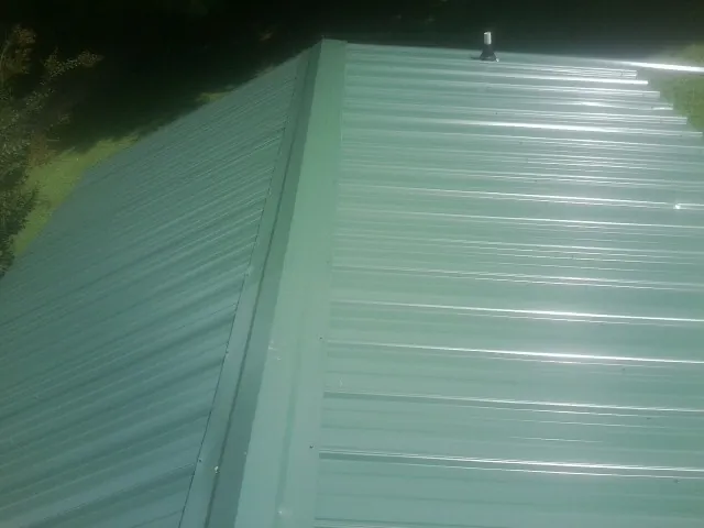 New green metal panels meeting at the ridge of a roof — Flat Roof Repair work by our crew in Wernersville