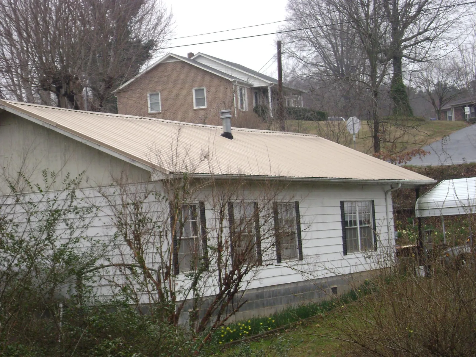 Tan metal roof on a white sided house set into a hillside — Commercial Roofing by Roofing Brothers in Wernersville